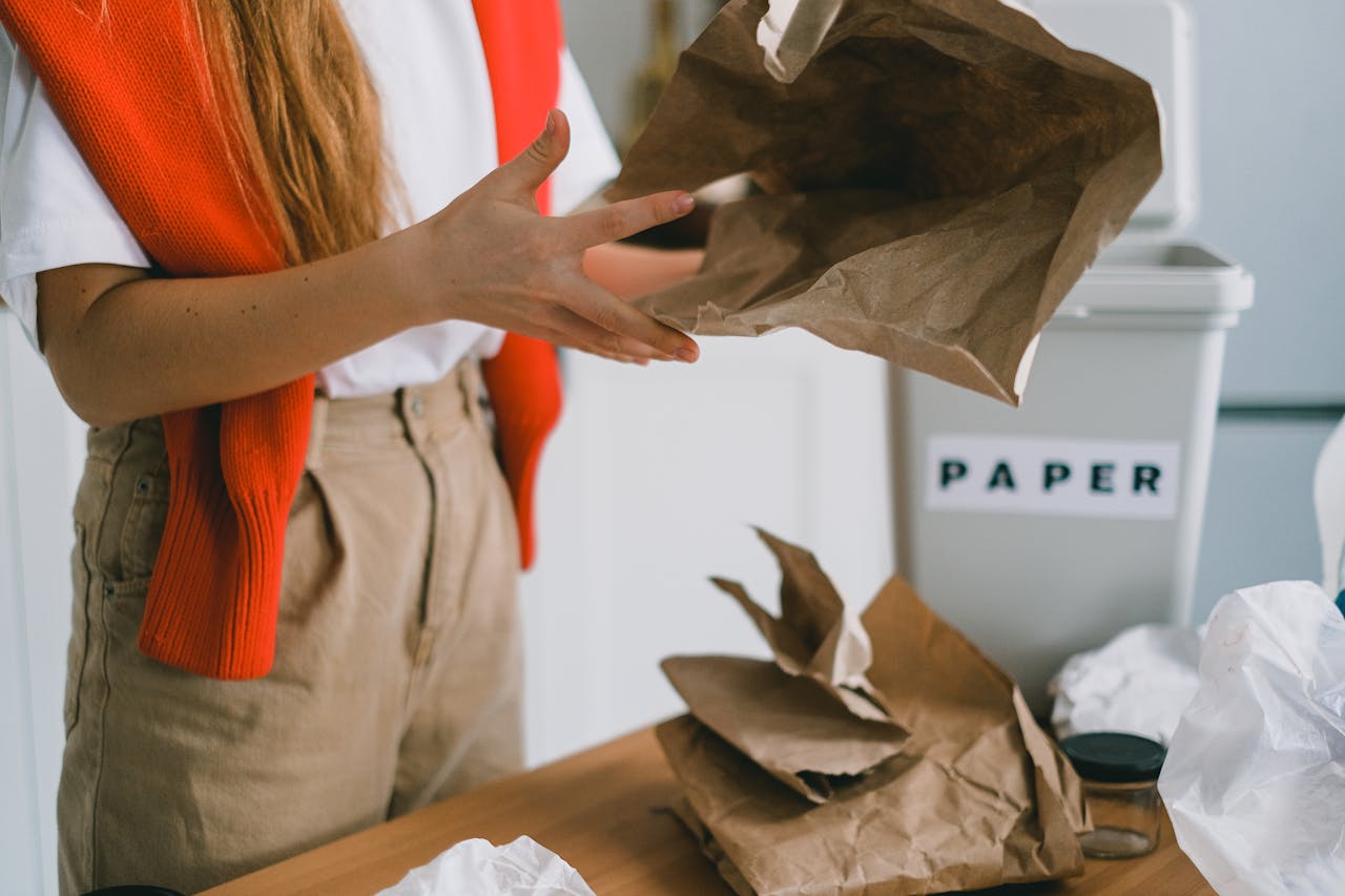 creative-03 Crop anonymous female standing at table and sorting paper trash from plastic packages and glass