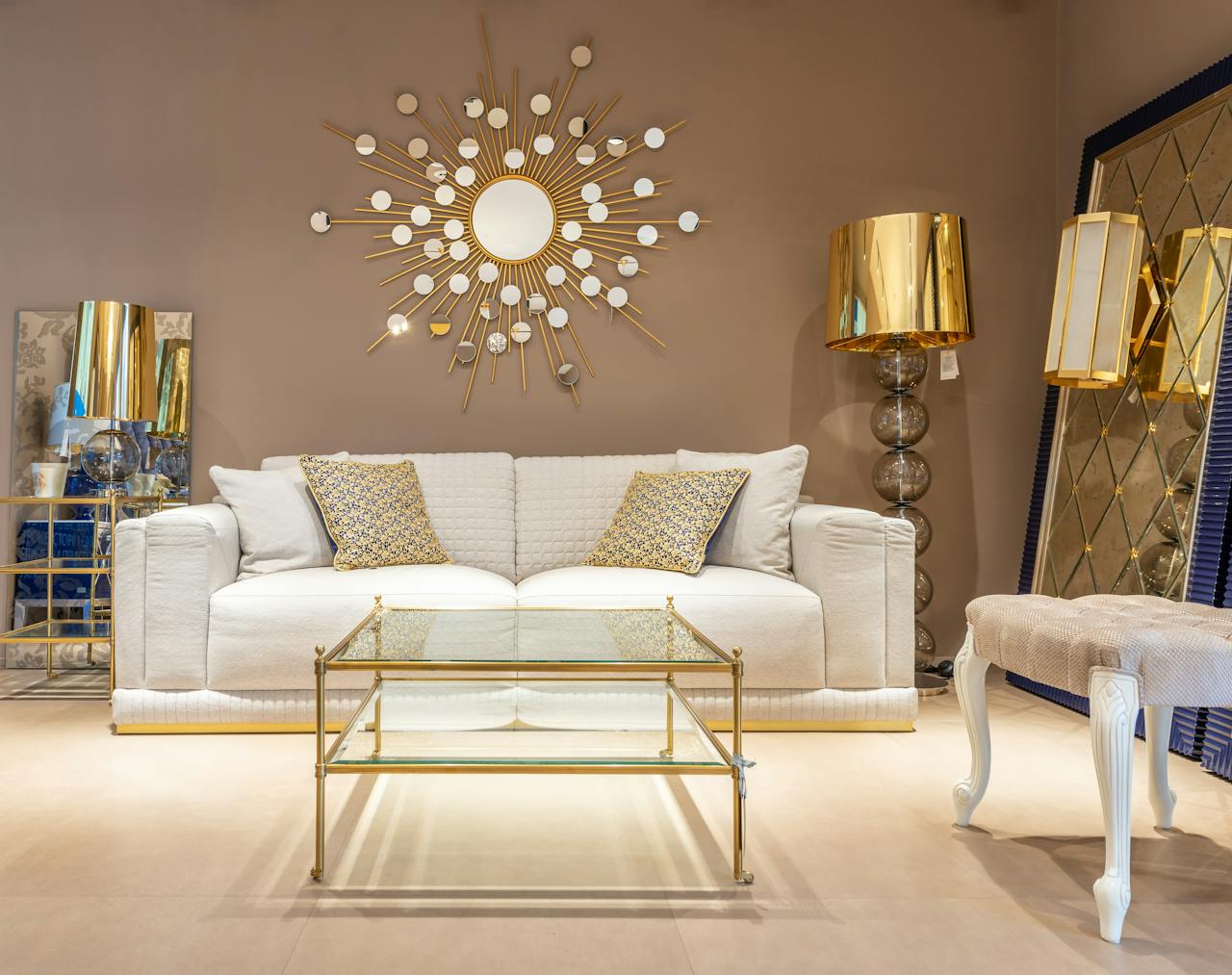 creative-02 Comfortable white sofa placed near glass table at wall with decorative elements in stylish living room with mirror and table lamp