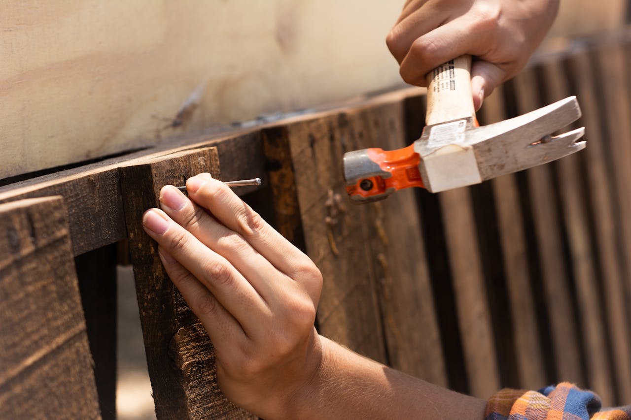 creative-01 A detailed image showing hands hammering a nail into wooden planks, emphasizing carpentry work.